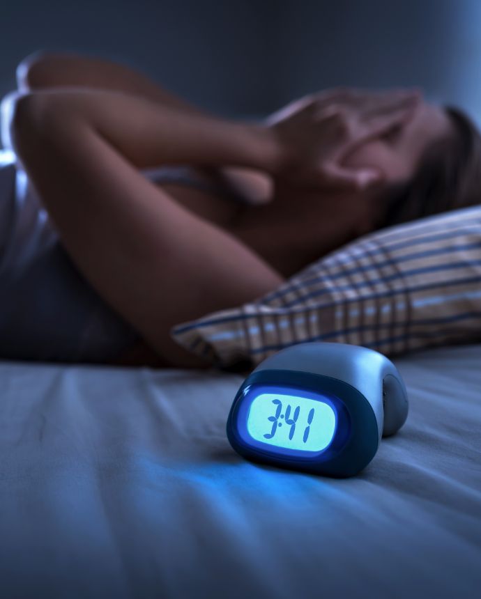 Woman laying awake in bed with an alarm clock showing the time as 3 41 AM